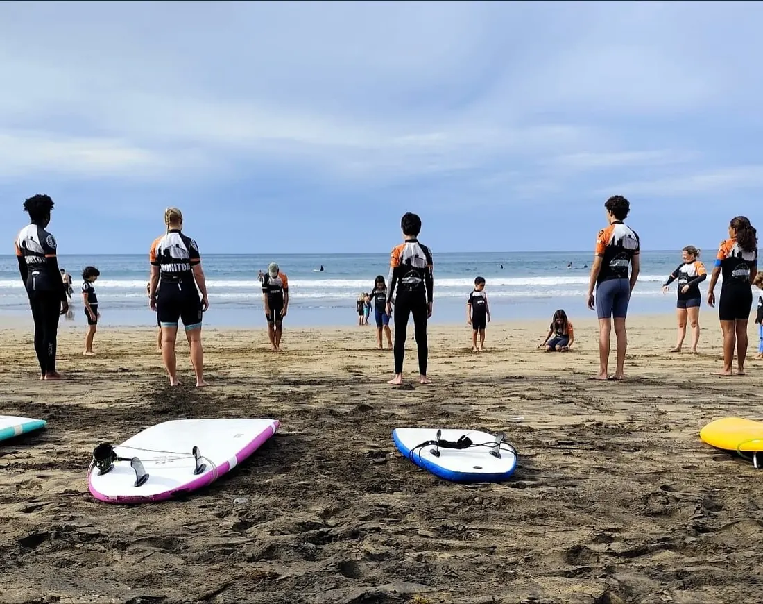 Alumnos calentando en la arena antes de la clase, con las tablas en el suelo