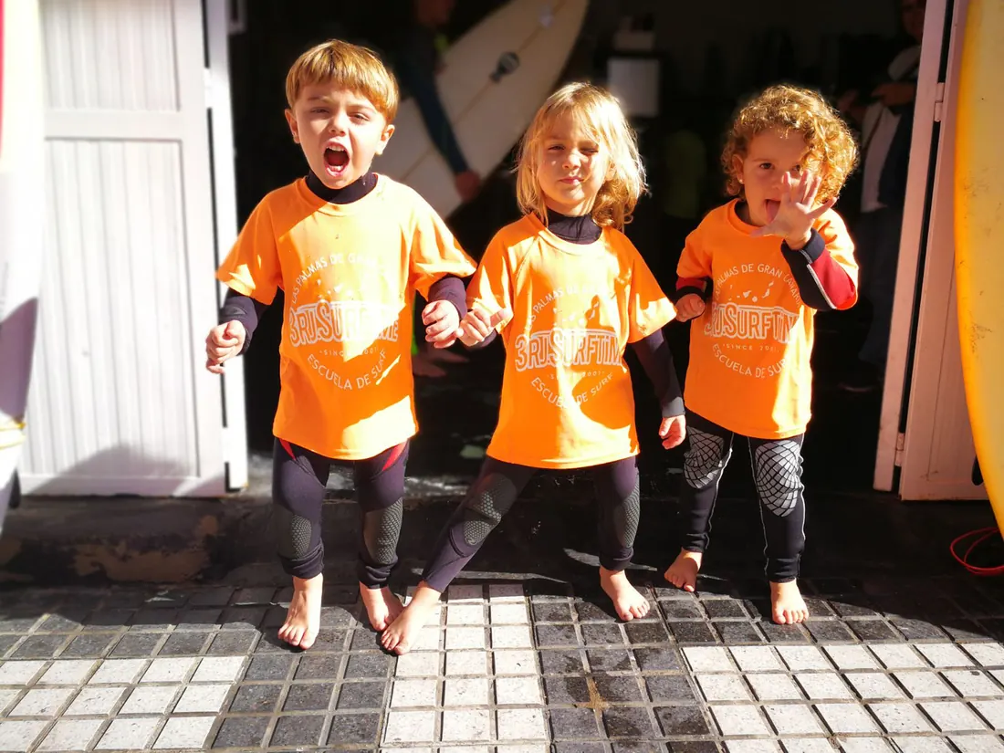 Tres niños con camisetas naranjas de la escuela en la puerta del local