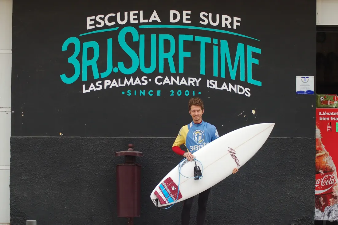 Fachada negra del local con el rótulo de 3RJ Surf Time en verde y un alumno con su tabla