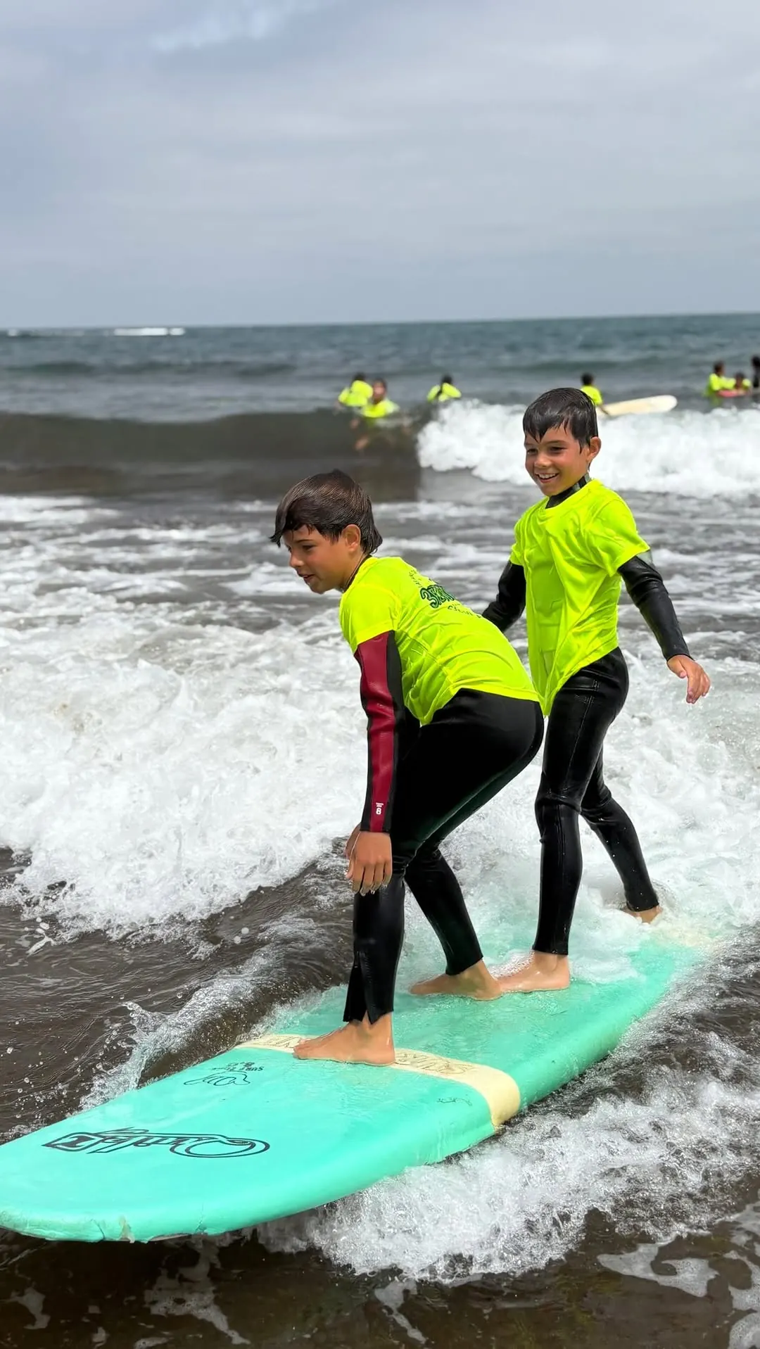Dos niños de pie en la misma tabla sobre la espuma en La Cícer